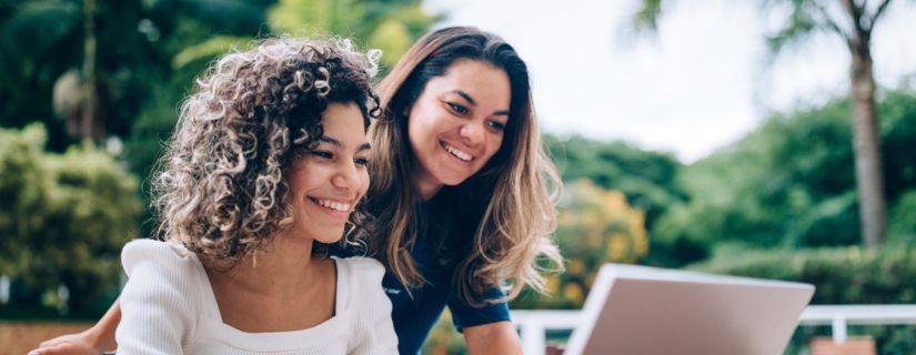 Two young wmen smiling over a laptop together.